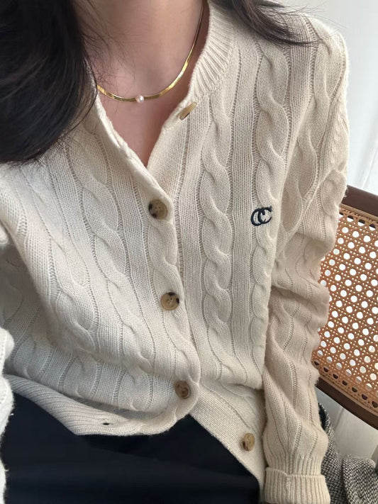 Beige cable knit cardigan with buttons worn by a person, sitting on a chair.