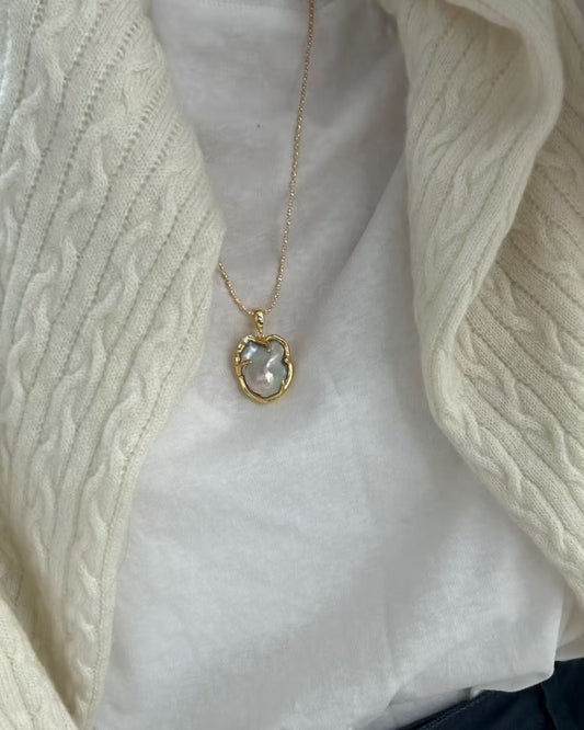 Necklace with a pendant worn by a person in a white shirt and beige cardigan.