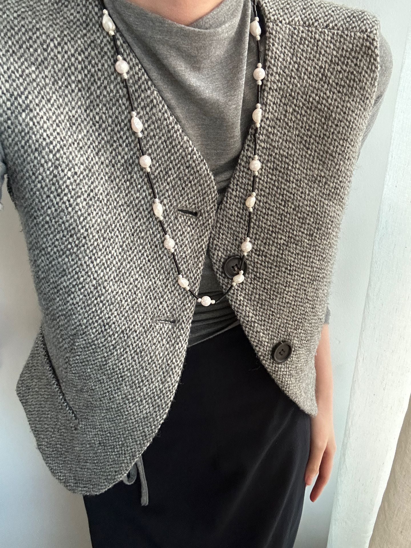 Gray textured blazer with pearl buttons worn by a person against a white background
