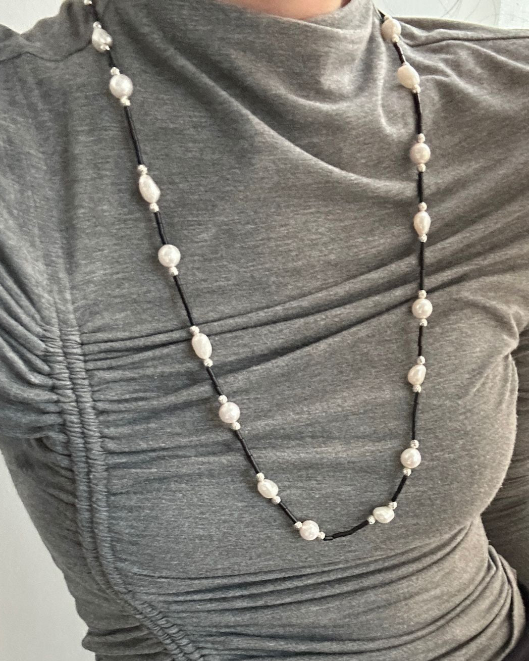 Person wearing a gray long-sleeve top with a pearl necklace