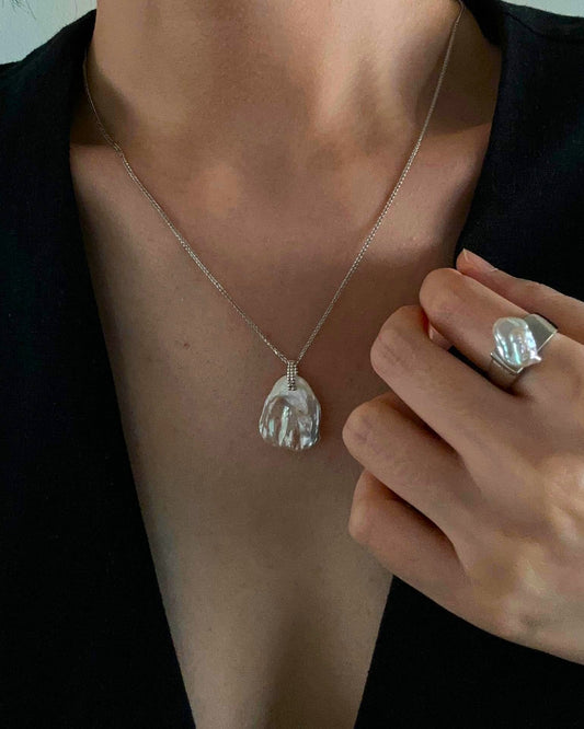 Person wearing a silver necklace with a paw-shaped pendant and a ring on a neutral background