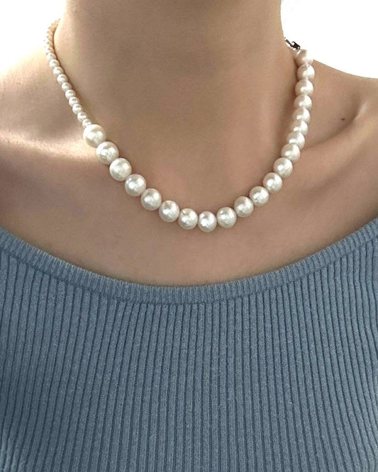 Person wearing a blue sweater and pearl necklace indoors