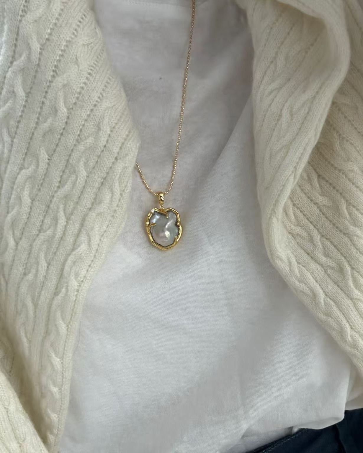 Necklace with a pendant worn by a person in a white shirt and beige cardigan.