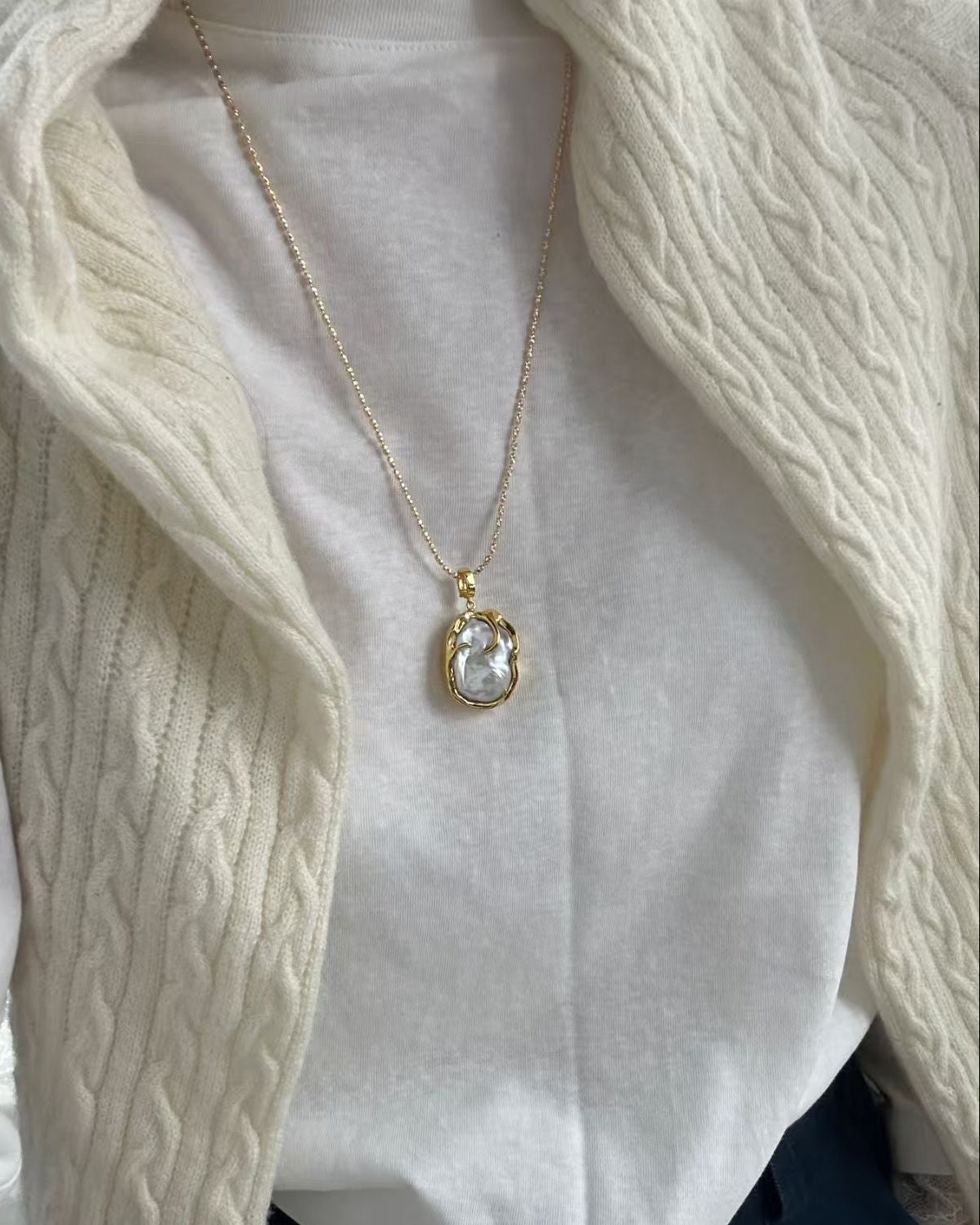 Necklace with a pendant worn over a white shirt and cream cardigan