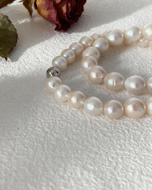Pearl necklace on a textured white surface with a dried rose and leaves.