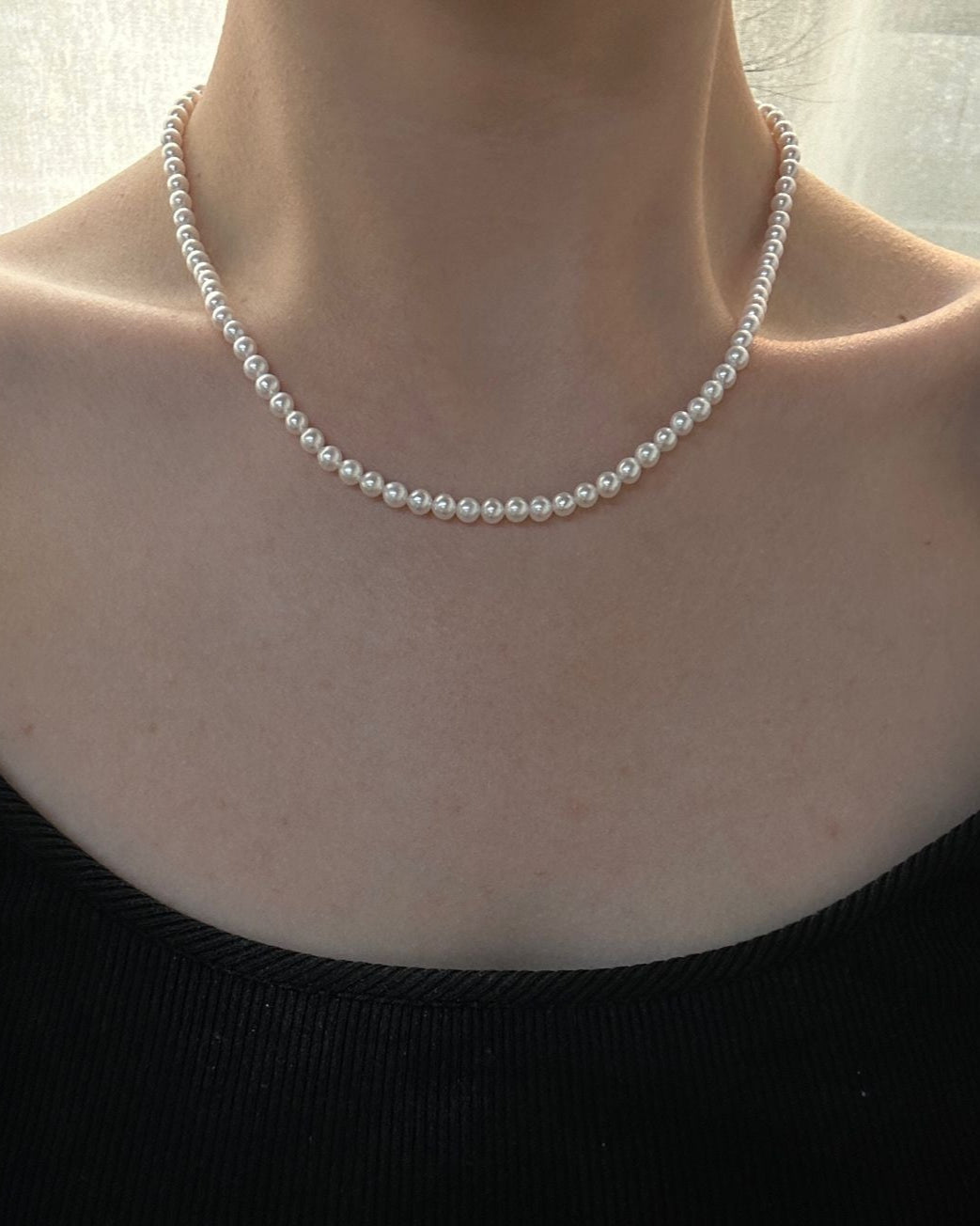 Person wearing a pearl necklace with a plain background
