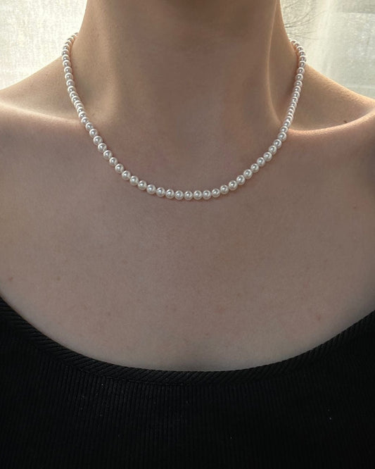 Person wearing a pearl necklace with a plain background
