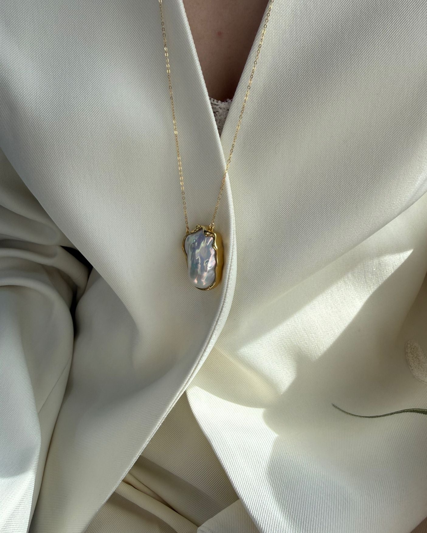 Close-up of a gold necklace with a large pendant on a white outfit