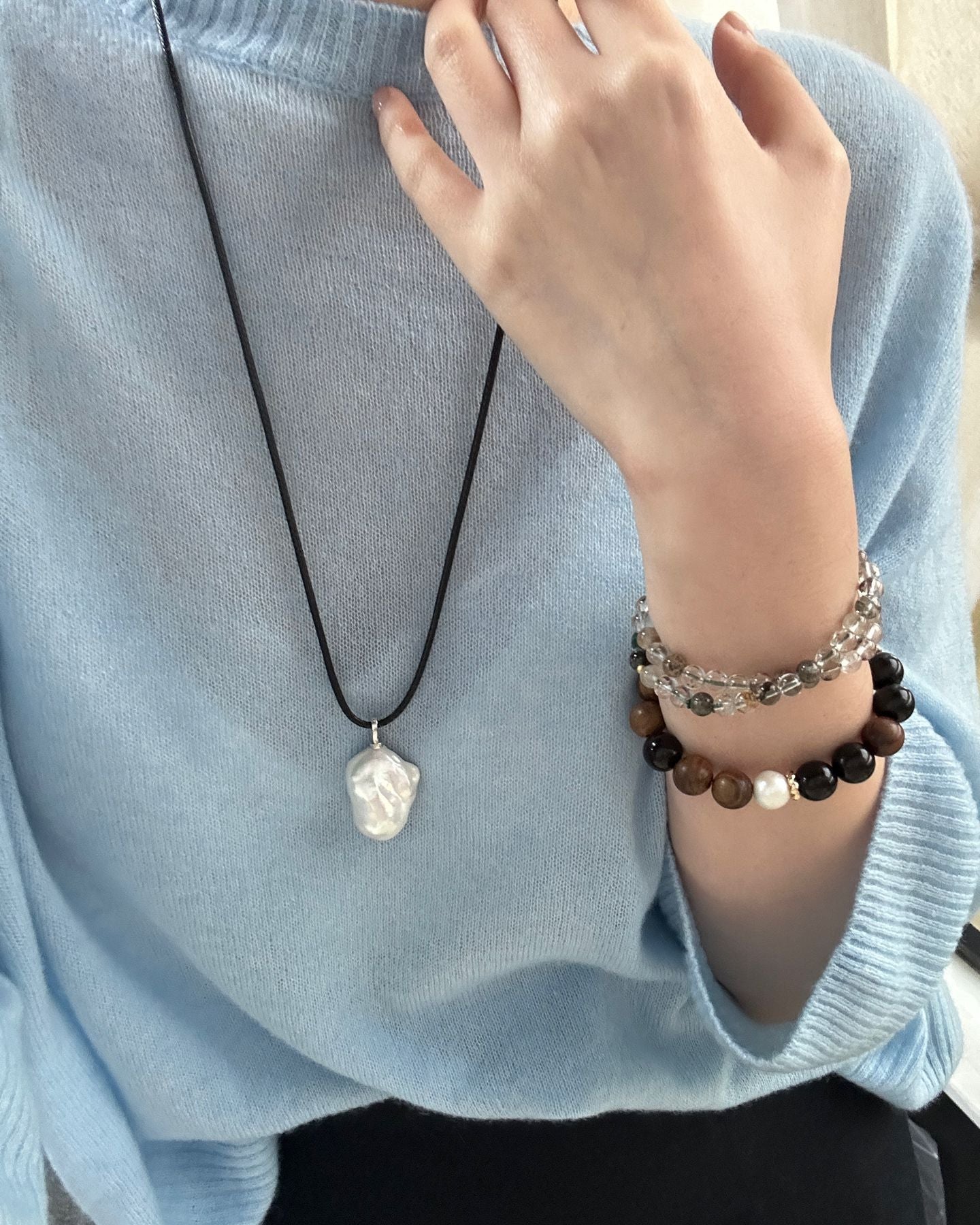Person wearing a necklace and bracelets on a light blue sweater