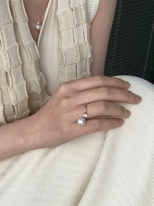 Person wearing a white sleeveless top and pants with a close-up of their hand holding a ring.