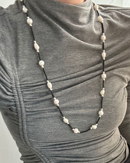 Person wearing a gray long-sleeve top with a pearl necklace