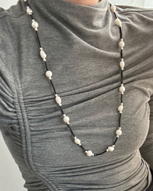 Person wearing a gray long-sleeve top with a pearl necklace