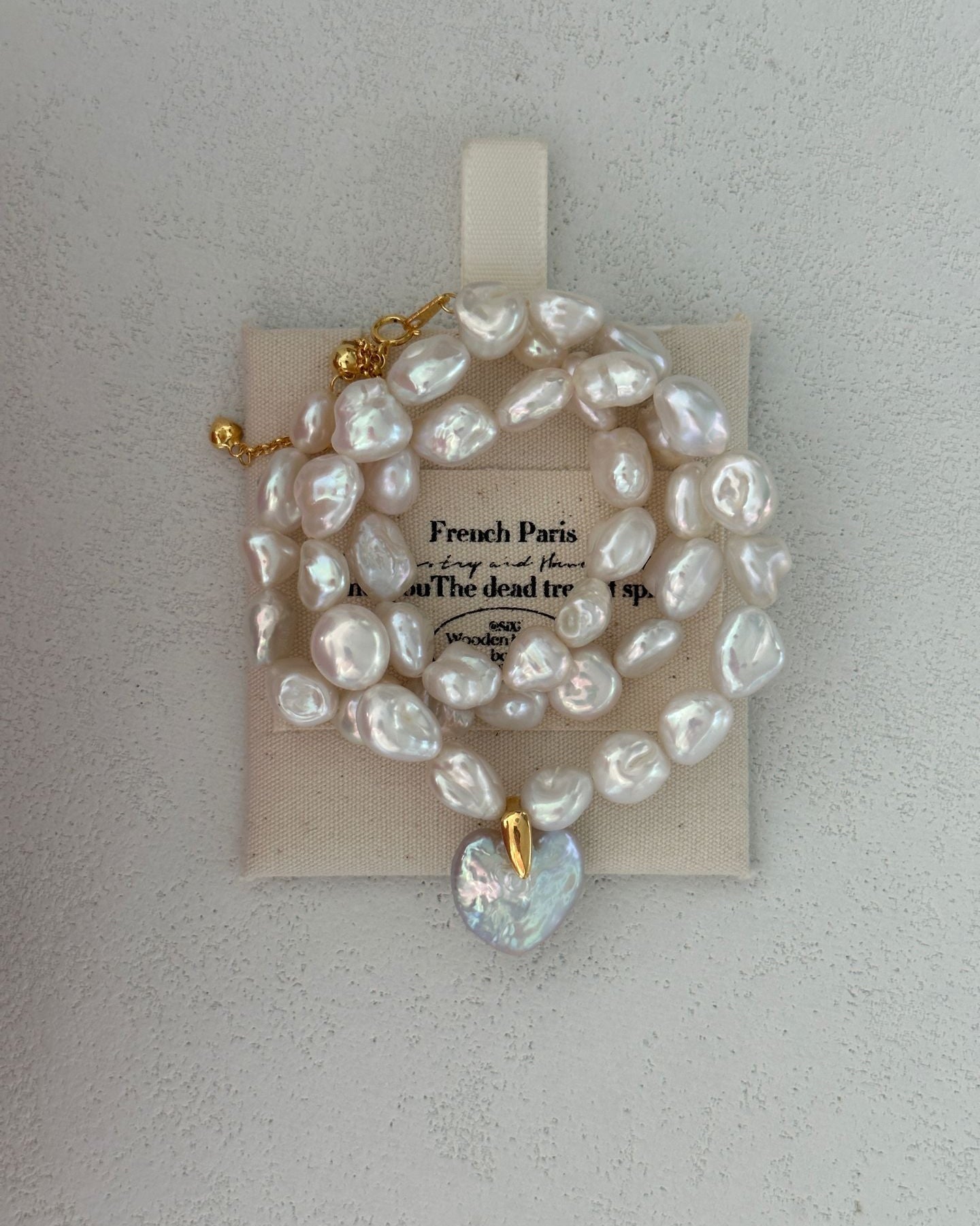 Pearl necklace with a heart-shaped pendant on a beige card against a light gray background