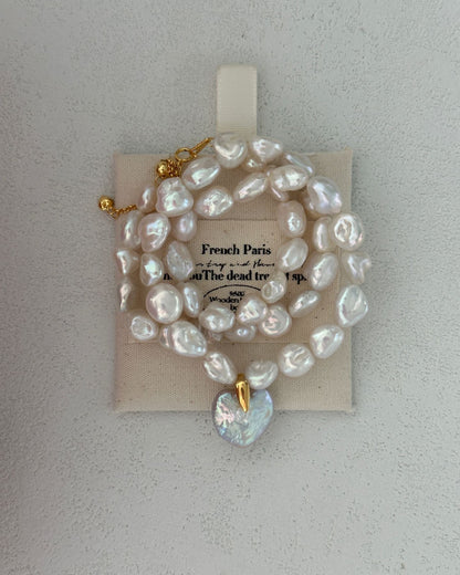 Pearl necklace with a heart-shaped pendant on a beige card against a light gray background