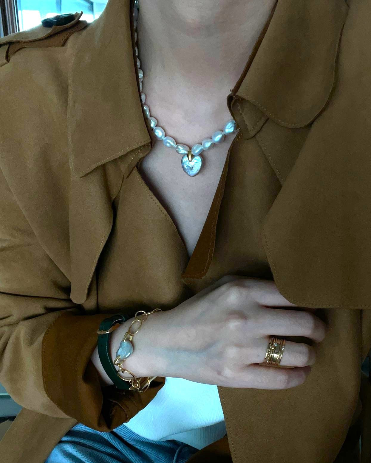 Person wearing a brown coat with visible jewelry including a necklace, bracelet, and ring.