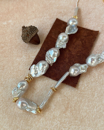 Pearl and gold beaded hair clip on a textured beige surface with an acorn.