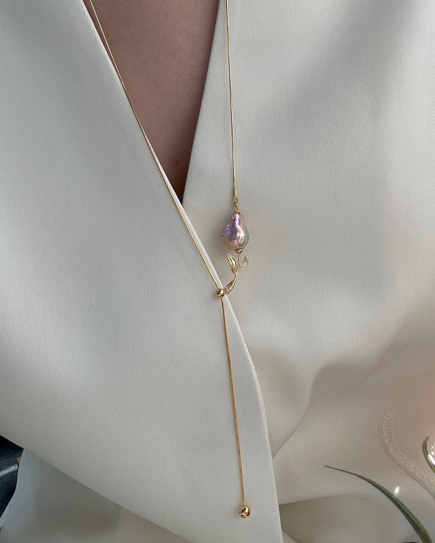 Gold necklace with a pink pendant on a white fabric background