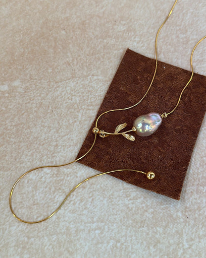 Gold necklace with a pearl pendant on a brown card against a beige background