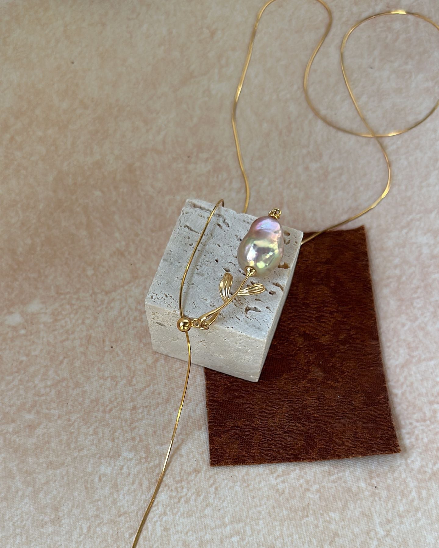 Gold necklace with a pendant on a textured beige surface