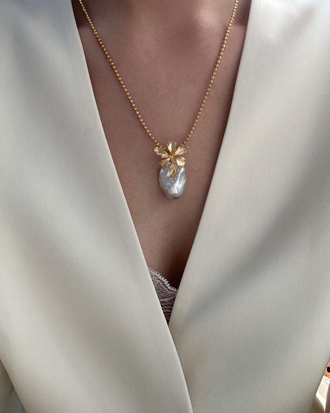Close-up of a gold necklace with a floral pendant on a white outfit