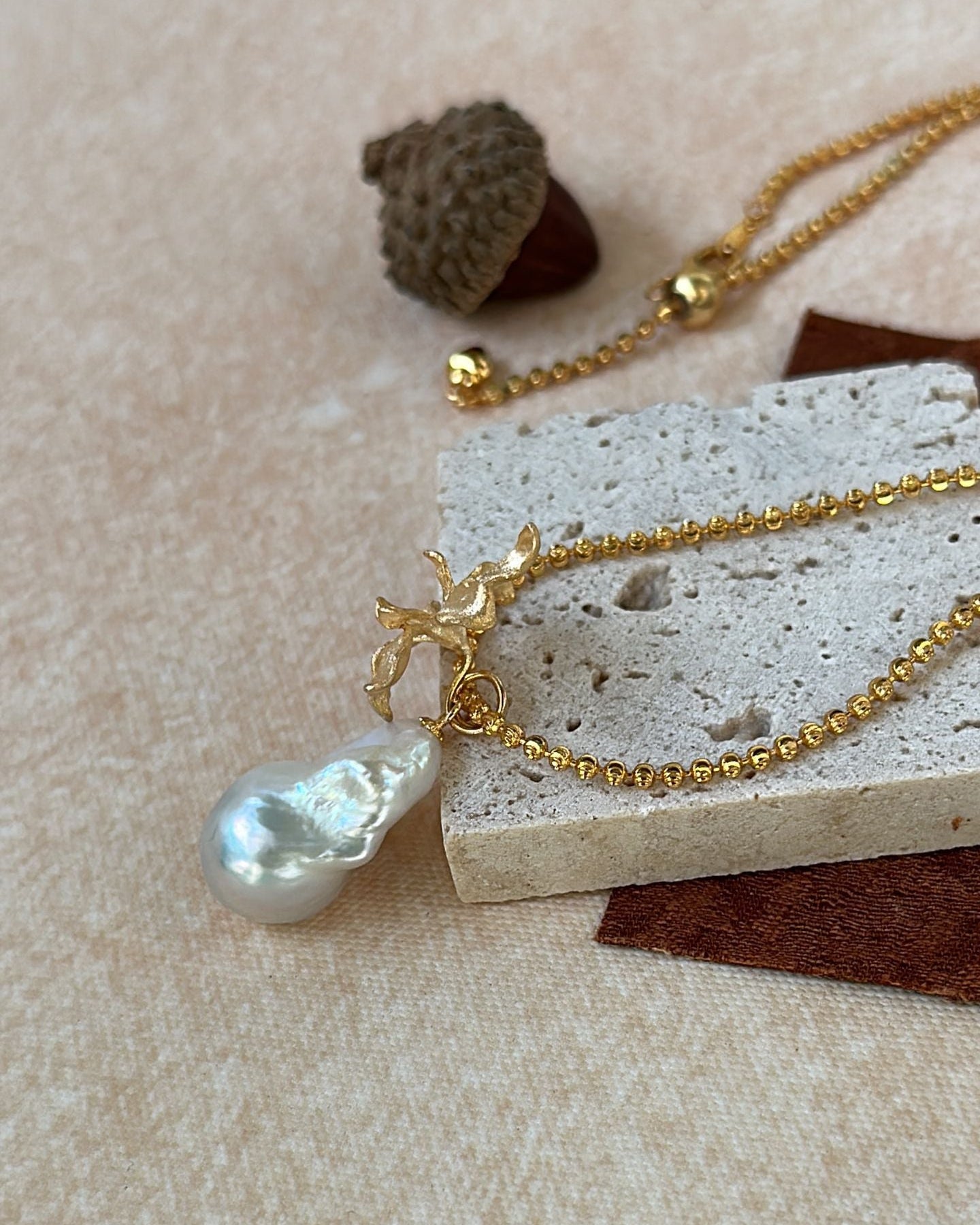 Gold necklace with a pearl pendant on a textured beige surface