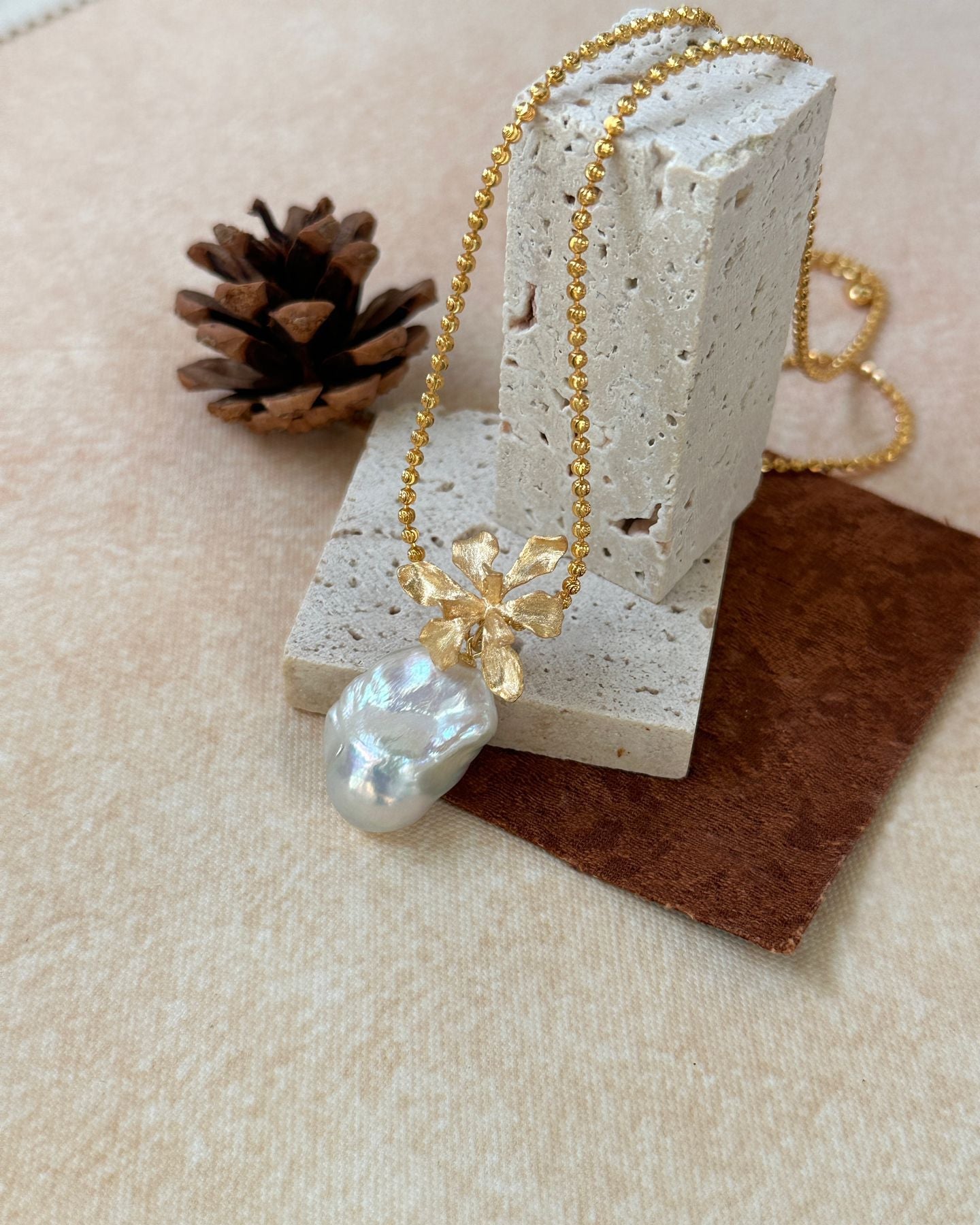 Gold necklace with a large pearl pendant on a textured surface