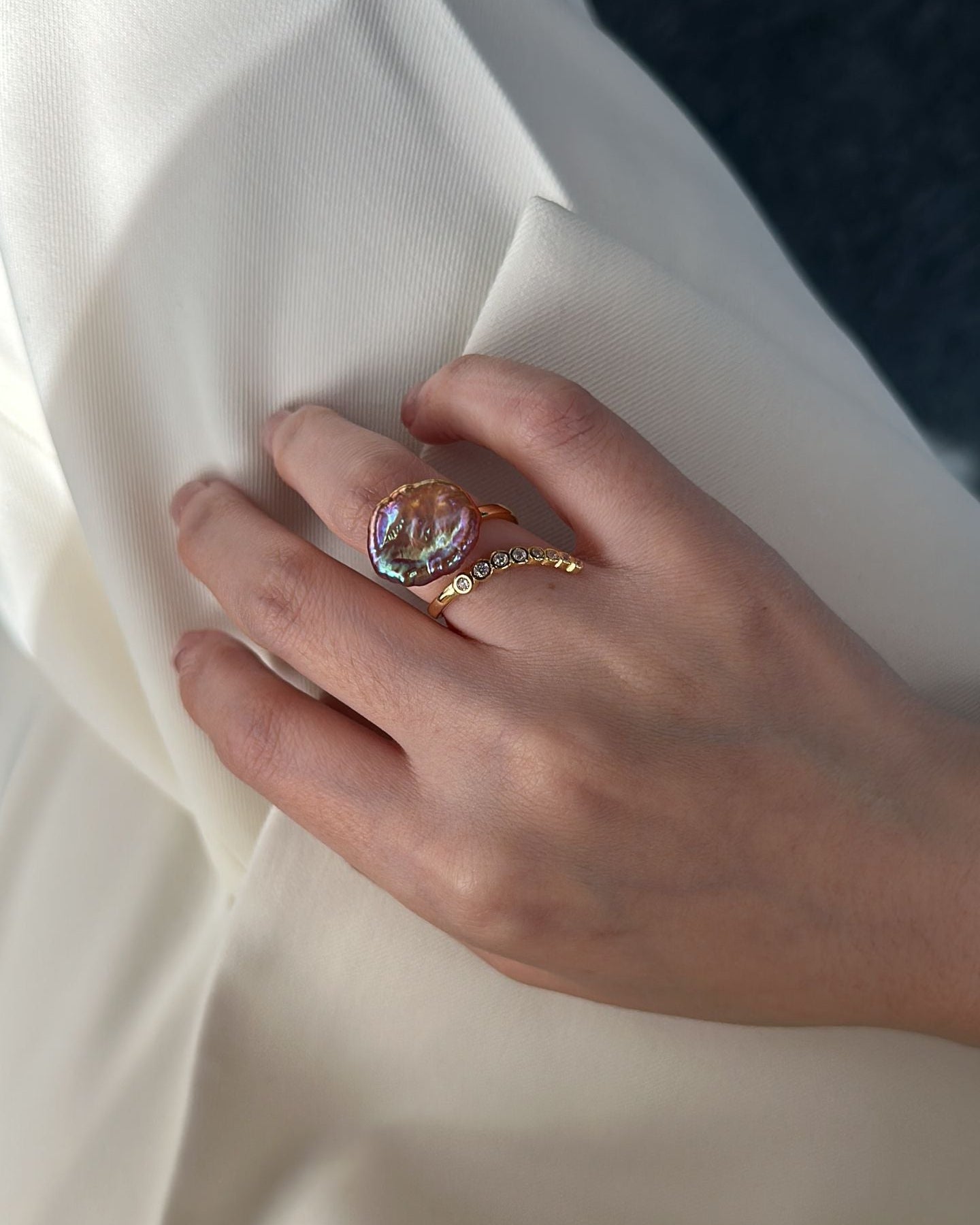 Hand wearing a ring with a clear gemstone on beige fabric