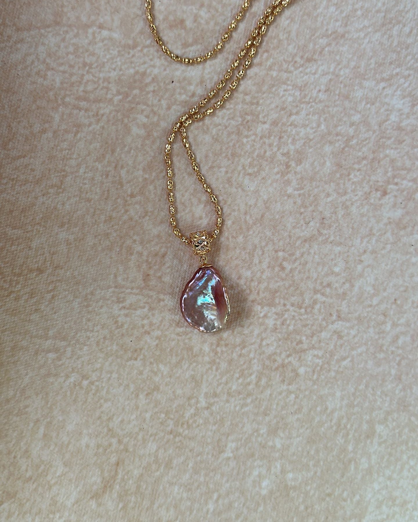 Gold necklace with a pink pendant on a beige background