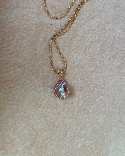 Gold necklace with a pink pendant on a beige background