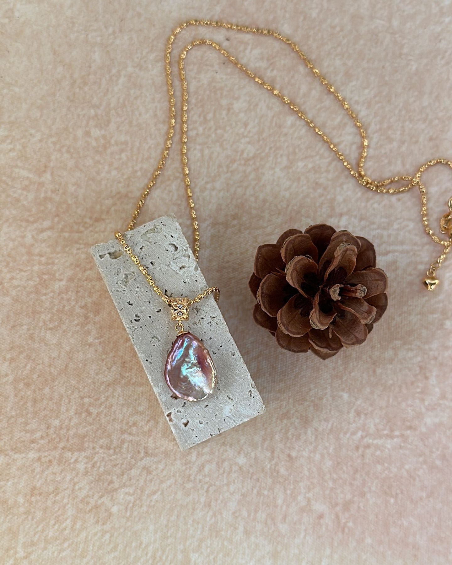 Necklace with a pendant on a concrete block next to a pine cone on a beige background