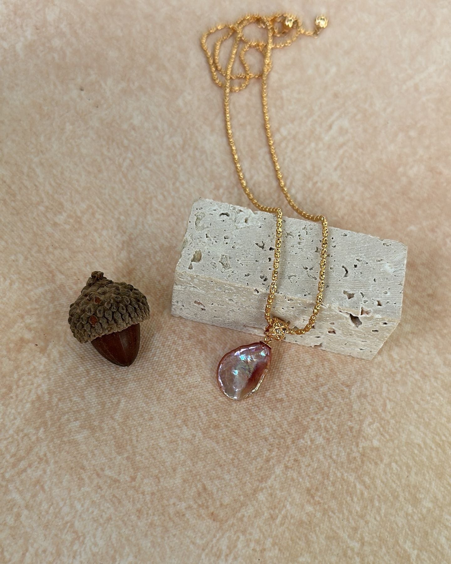 Necklace with a pendant on a textured beige surface next to an acorn