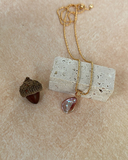 Necklace with a pendant on a textured beige surface next to an acorn