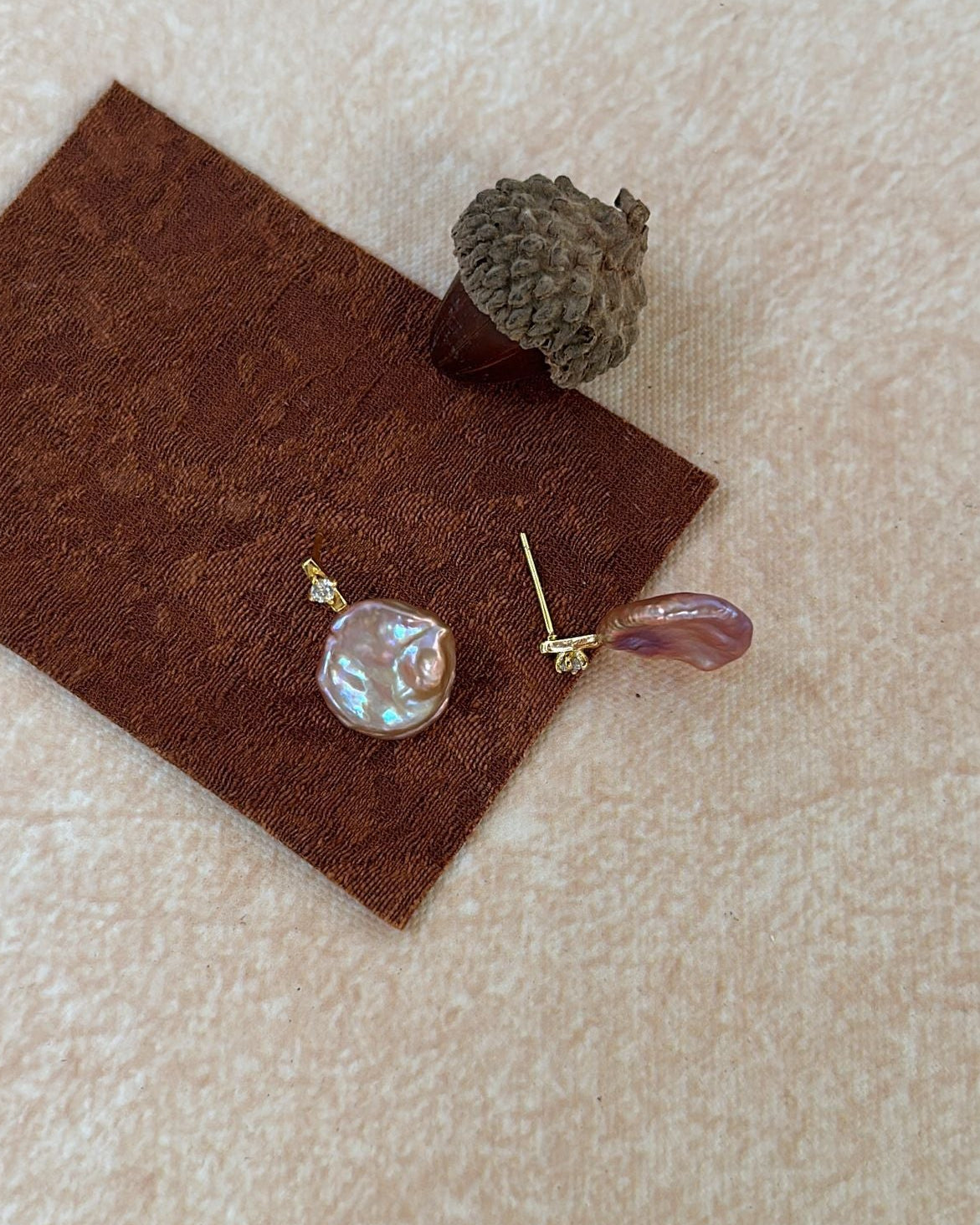 Two earrings on a brown felt pad with a beige background