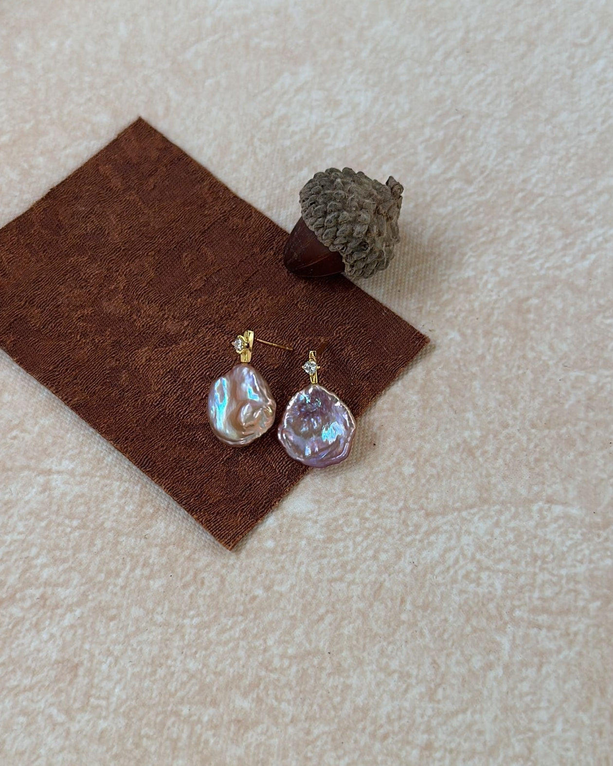 Two earrings on a brown felt pad with a textured beige background
