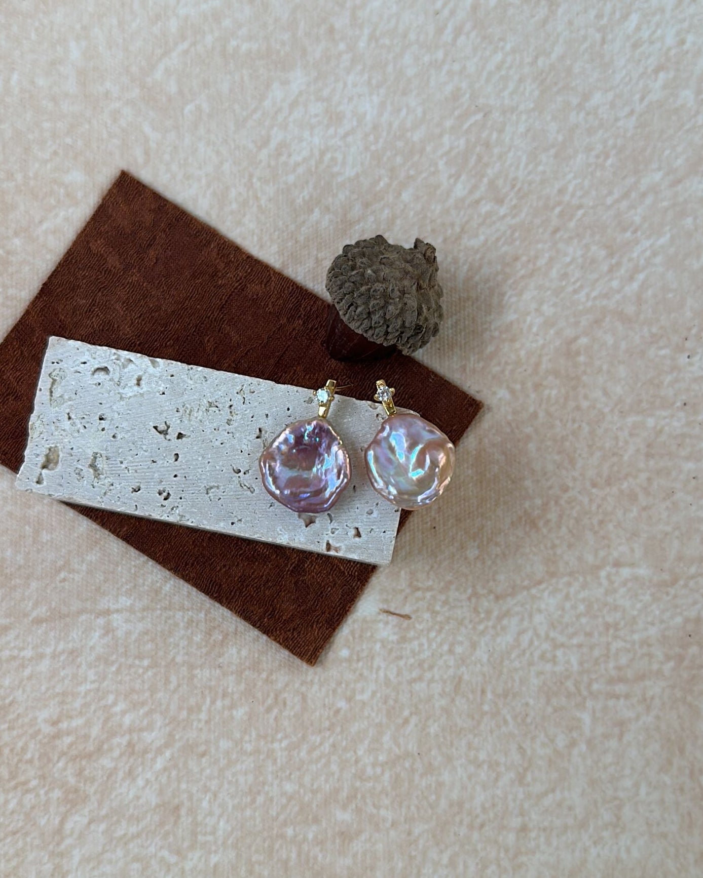 Pair of earrings on a textured surface with a small pine cone.