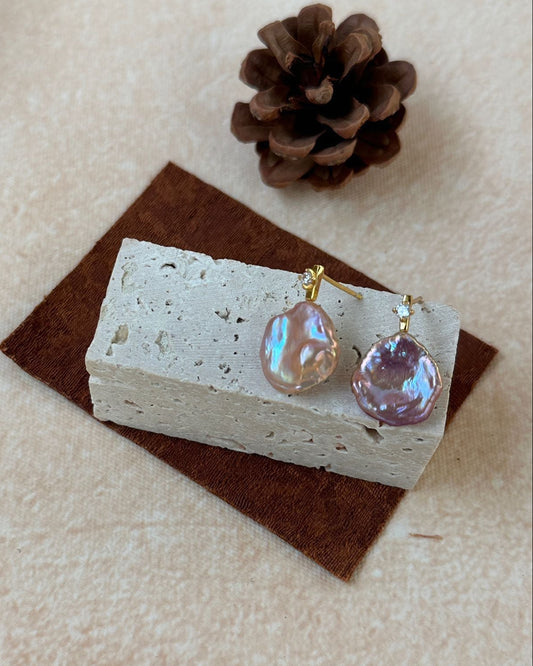 Pair of teardrop-shaped earrings on a stone block with a pine cone on a beige background