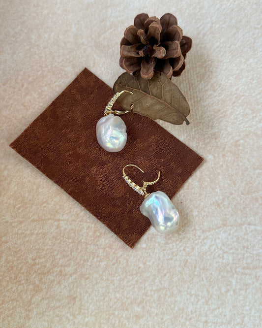 Pearl earrings on a brown square with a pine cone and leaf on a beige background