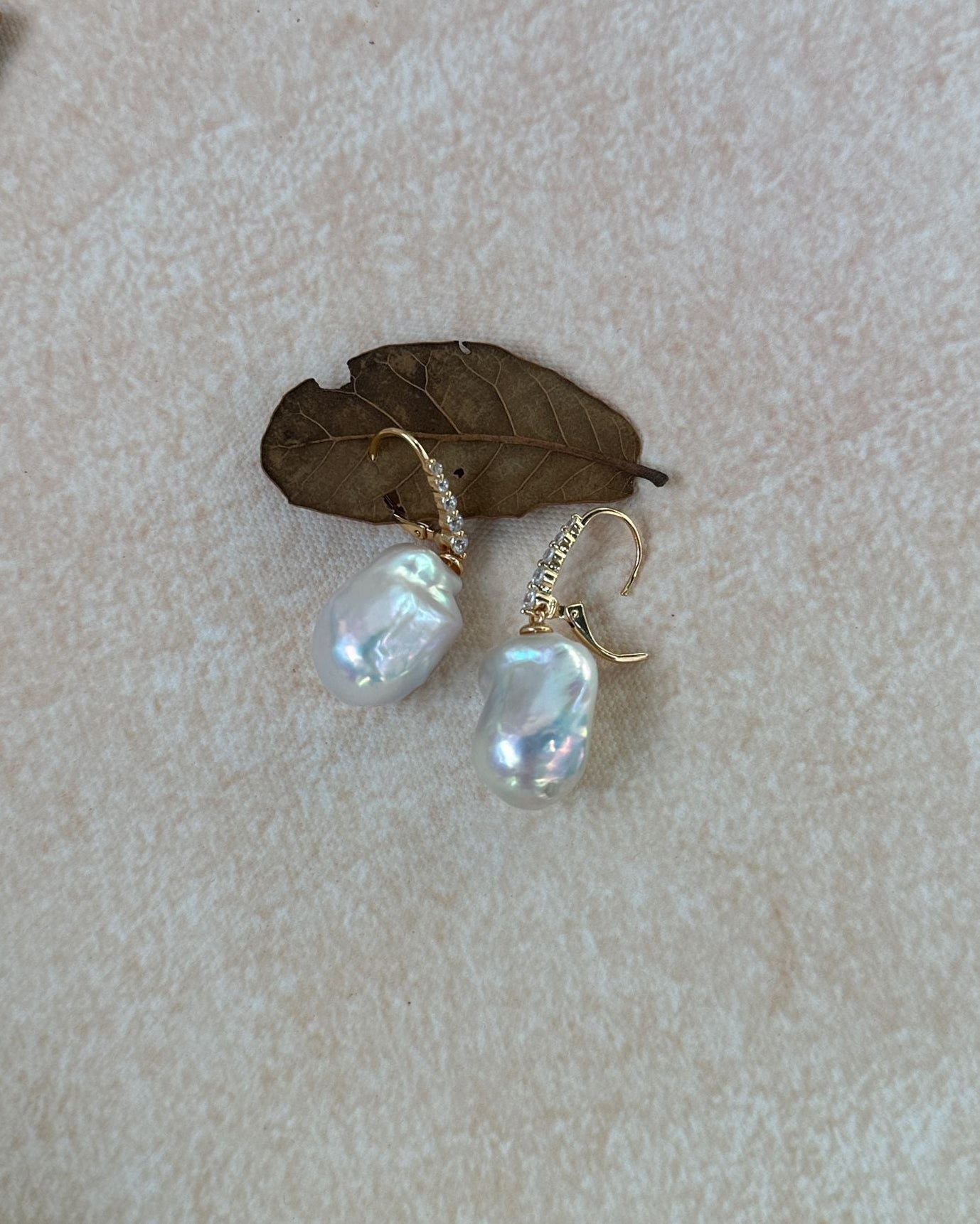 Pearl earrings on a textured beige surface with a leaf