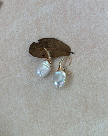 Pearl earrings on a textured beige surface with a leaf
