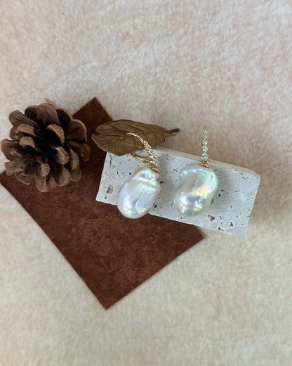 Pearl earrings on a card with a pine cone and leaf on a beige background