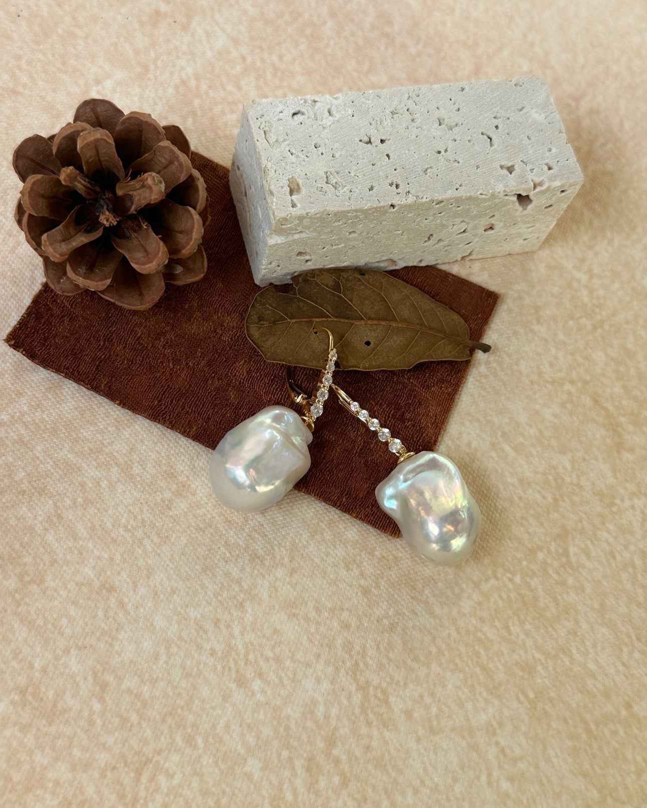 Pearl earrings with a brick and pine cone on a beige surface