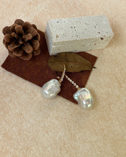 Pearl earrings with a brick and pine cone on a beige surface