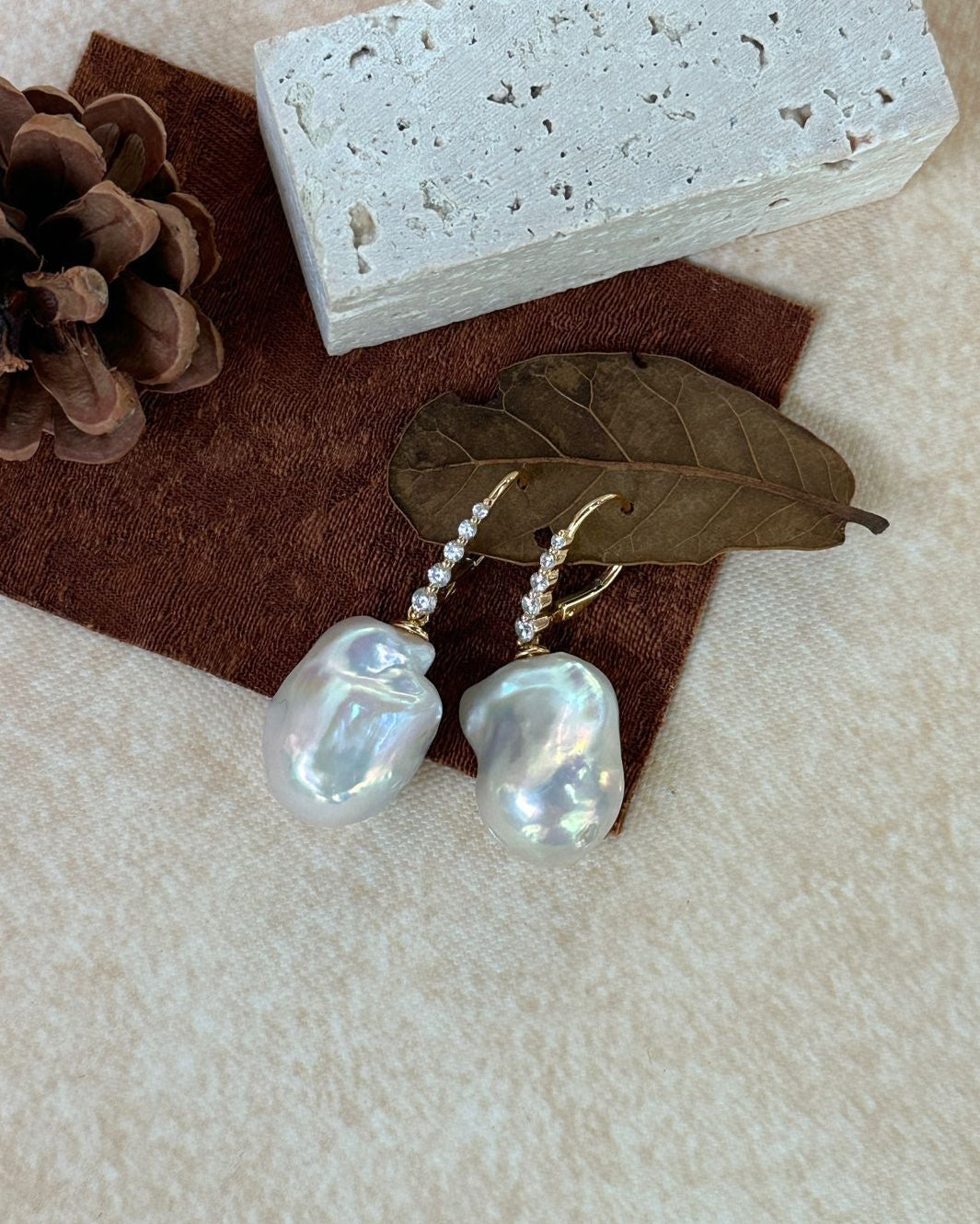 Pearl earrings with a pine cone and leaf on a textured surface