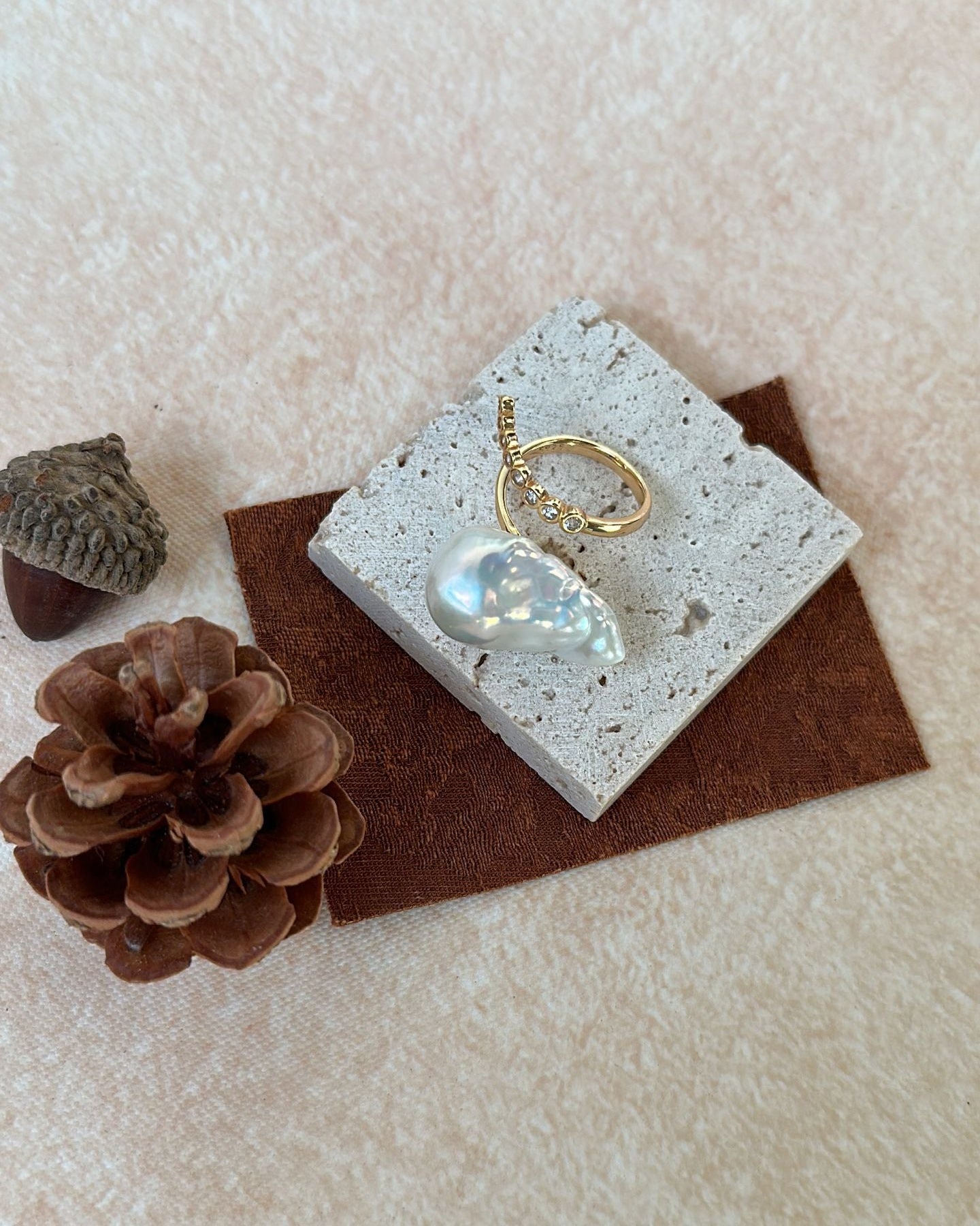 Gold ring with a moonstone on a textured surface with pine cones and a pine cone.