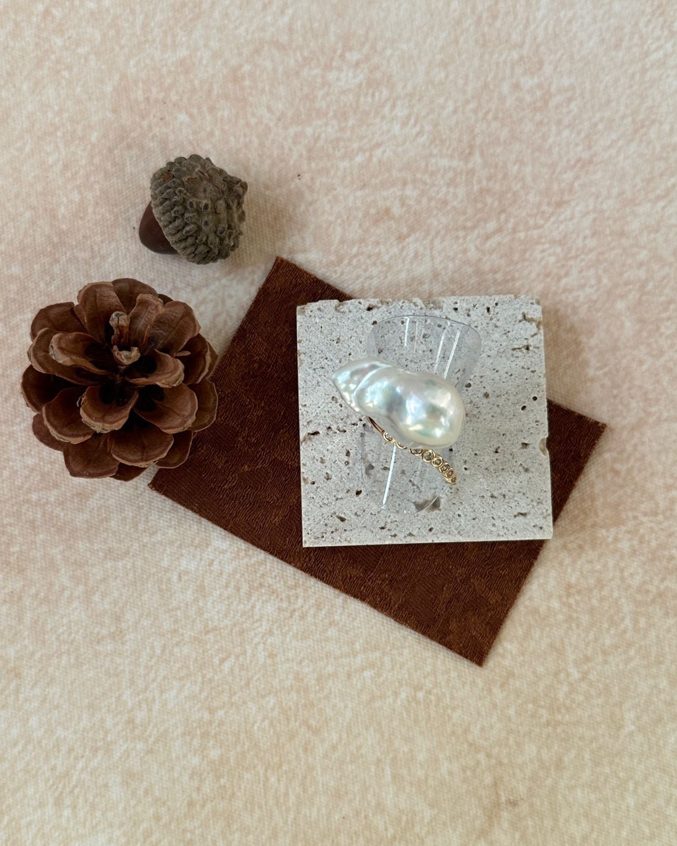 Pearl earring on a card with a pine cone and pinecones on a beige surface