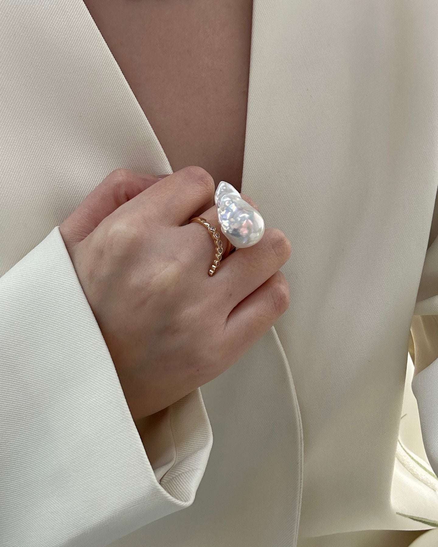 Close-up of a hand wearing a gold ring with a large pearl on a neutral background