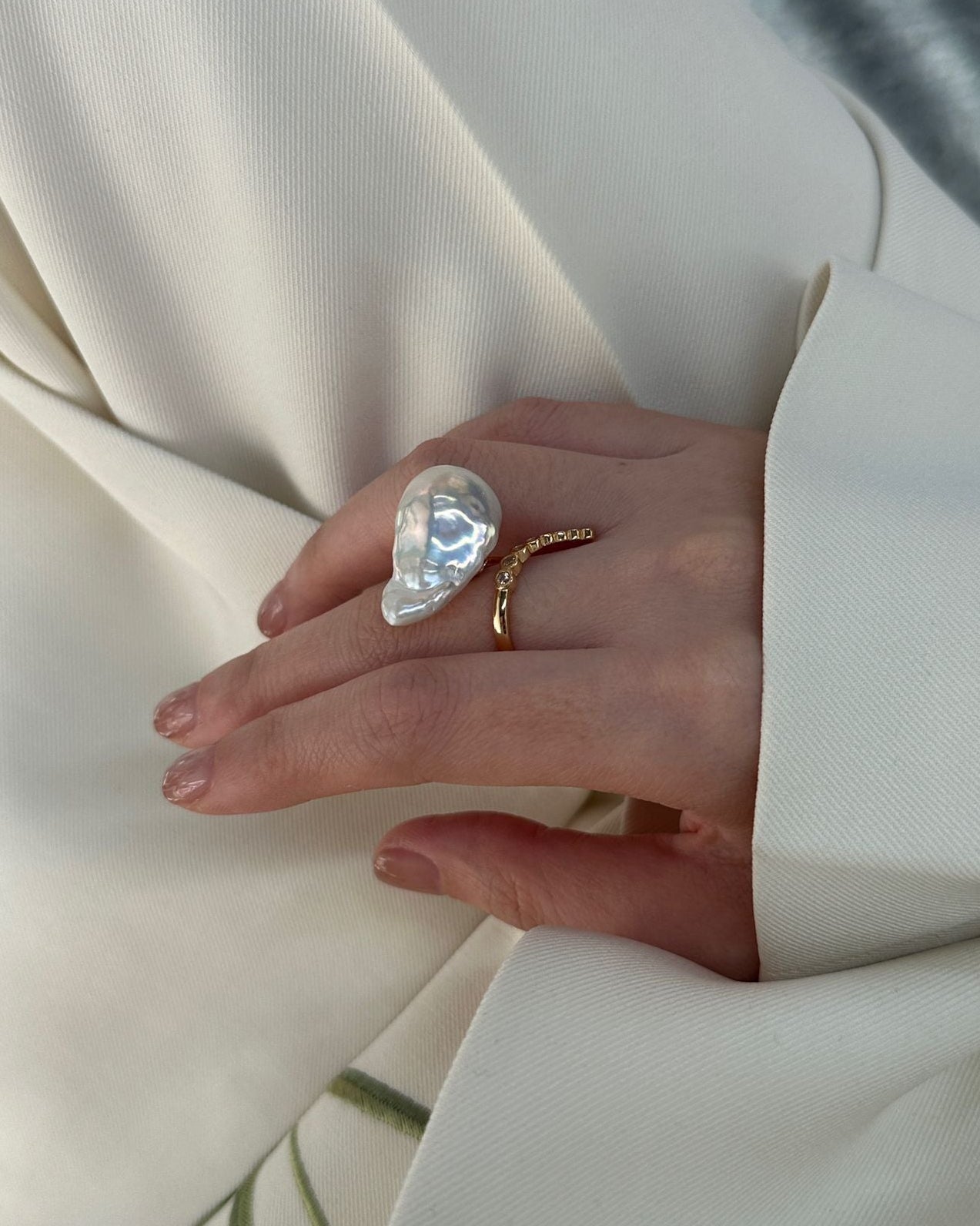 Hand wearing a large pearl ring with a white coat background