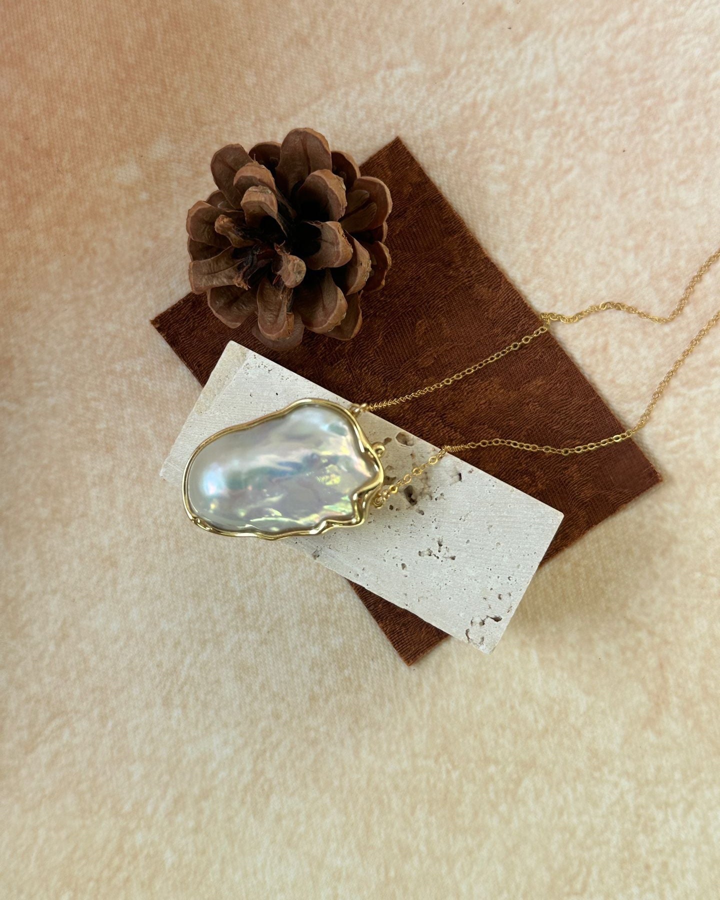 Necklace with a large, faceted pendant on a textured surface with a pine cone.