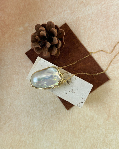 Necklace with a large, faceted pendant on a textured surface with a pine cone.
