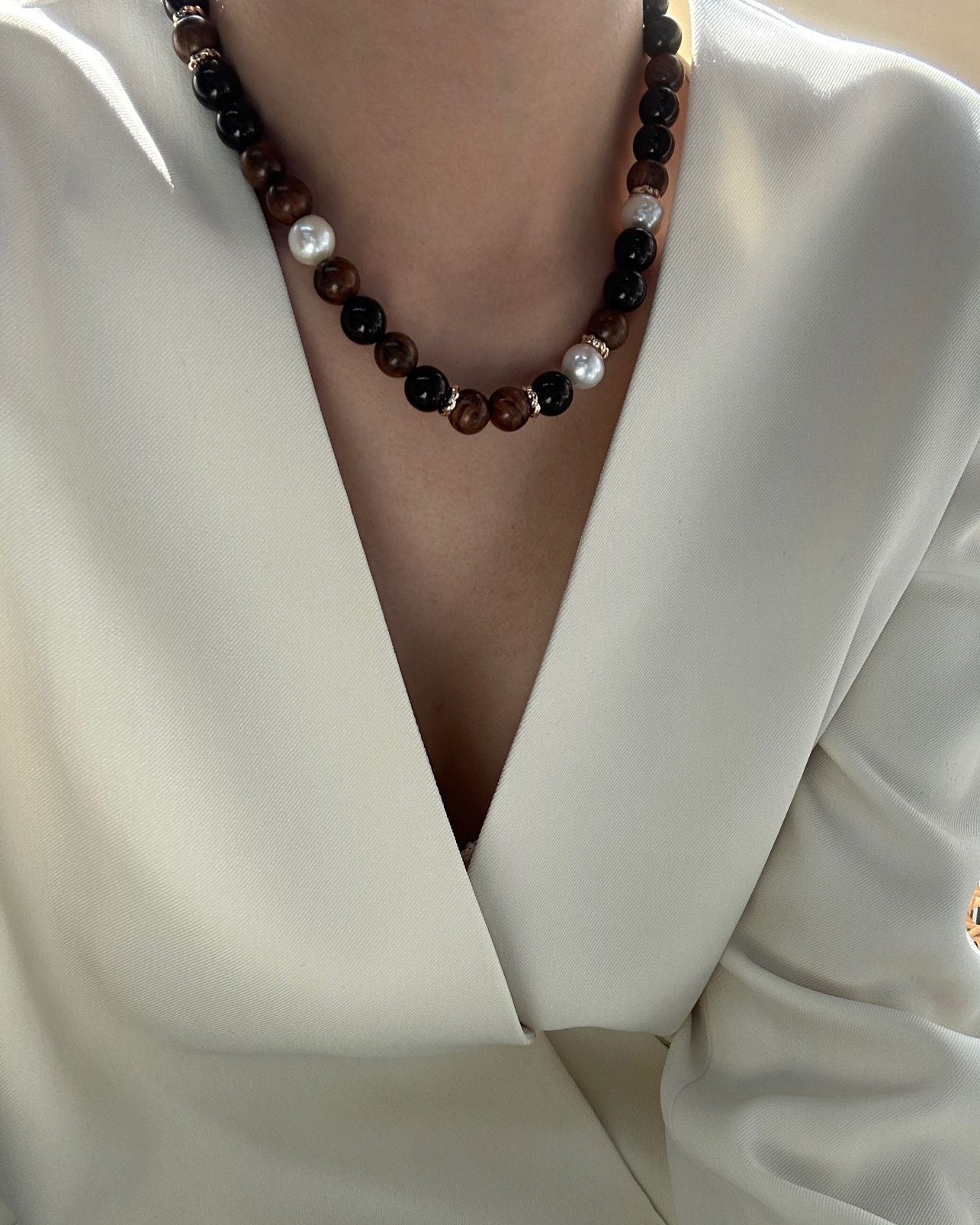 Close-up of a person wearing a white blouse with a deep neckline and a dark beaded necklace.